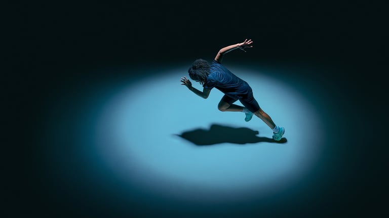 Female teenager athlete sprinting with strong shadow under spotlight in minimal dark studio, concept of speed training and performance optimization